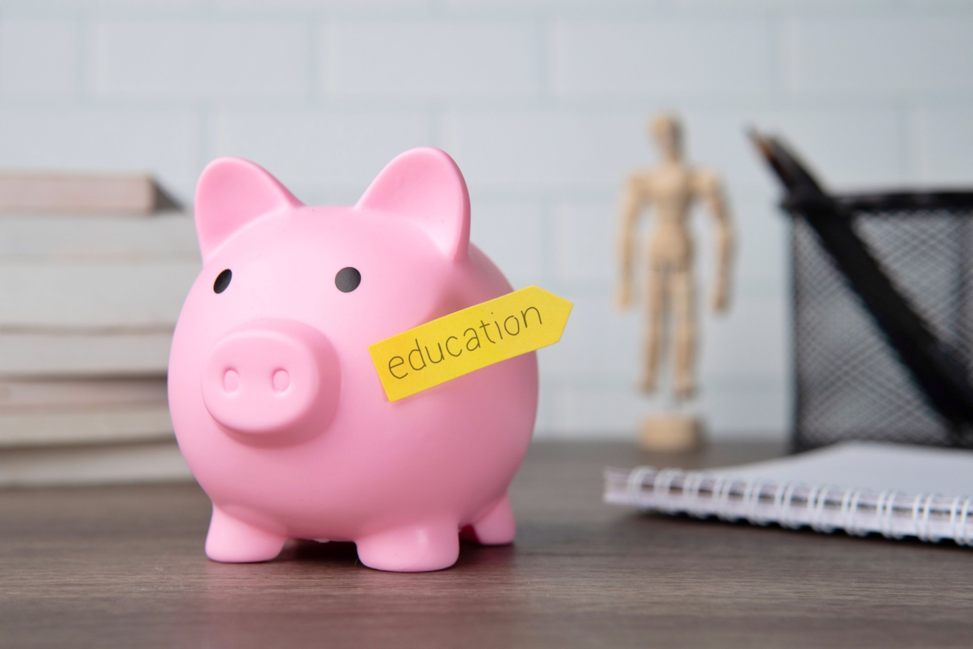 A pink piggy bank with a yellow sticky note labeled education attached to its side.