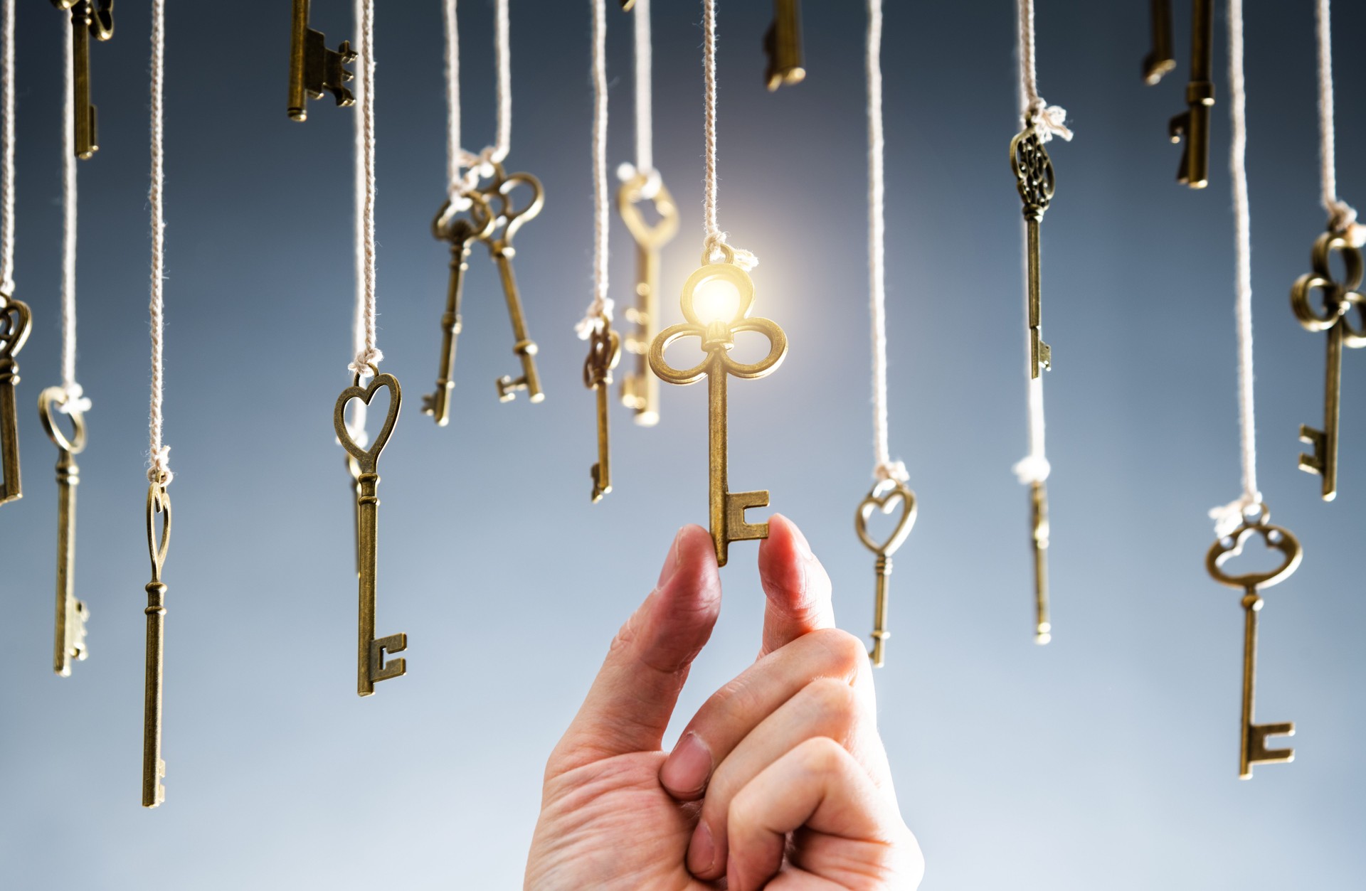 Hand choosing the right key to success from hanging vintage keys on dark background